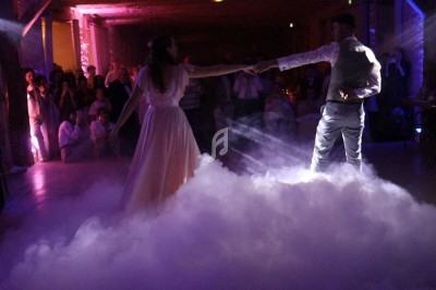 Un couple danse sur une piste enveloppée de fumée et éclairée par des lumières colorées, devant un public.