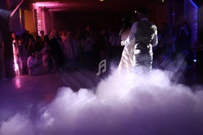 Un couple danse au milieu d'une piste enveloppée de fumée, sous des lumières tamisées, devant des invités.