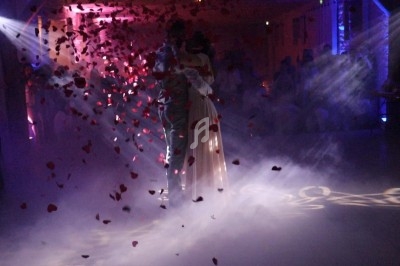 Un couple danse au milieu d'une piste entourée de fumée et de pétales de rose sous un éclairage tamisé.