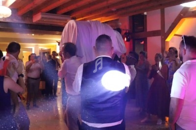 Des personnes dansent et célèbrent dans une salle éclairée, avec un homme porté sur les épaules au centre.