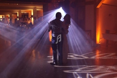 Un couple danse sous des éclairages tamisés et des faisceaux lumineux dans une salle de réception.