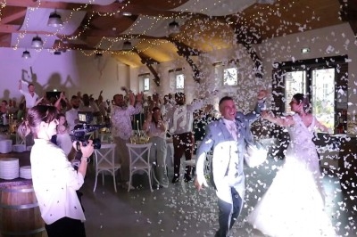 Un couple de mariés entre dans une salle décorée, entouré d'invités lançant des confettis sous des lumières festives.