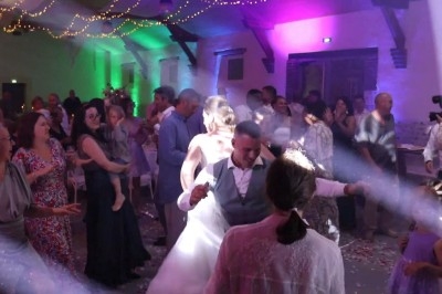 Des invités dansent dans une salle éclairée par des lumières colorées lors d'une fête ou d'un mariage.