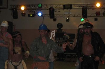 Des personnes déguisées, dont un ouvrier et un motard, dansent sous des éclairages colorés dans une salle.