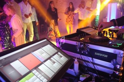Un DJ mixe de la musique lors d'une soirée dansante, avec des invités sur la piste et des lumières colorées.
