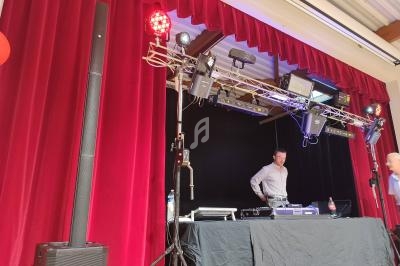 Un DJ se tient derrière une table de mixage sur une scène avec rideaux rouges et éclairages de spectacle.