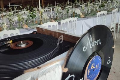 Platines vinyles avec un panneau ’Mon bar à vinyles’ devant une salle décorée pour un événement avec tables dressées.
