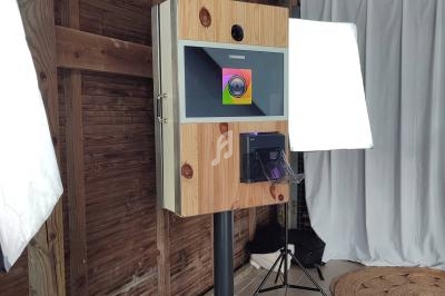 Borne photo en bois avec écran tactile, installée dans un espace intérieur avec éclairage et rideaux en arrière-plan.