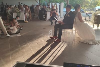 Un couple assis lors d'une réception de mariage en plein air, entouré d'invités et éclairé par la lumière du soleil couchant.