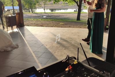 Vue depuis une table de mixage sur une cérémonie en extérieur près d'un lac, avec des invités debout au coucher du soleil.