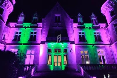 Façade d'un bâtiment ancien éclairé par des lumières violettes et vertes, de nuit.