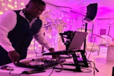 Un DJ en costume utilise une table de mixage et un ordinateur dans une salle décorée avec des lumières roses.