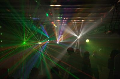 Effets lumineux colorés et rayons laser éclairant une salle sombre avec des silhouettes de personnes.