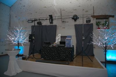 Scène de DJ installée dans une salle avec éclairage décoratif, tables et rideaux gris en arrière-plan.