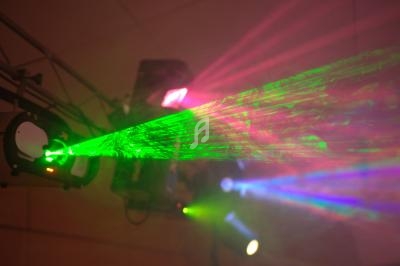 Faisceau laser vert projeté dans une pièce sombre avec des lumières colorées en arrière-plan.