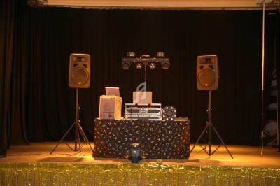 Table de mixage avec ordinateur portable, enceintes et éclairages sur une scène décorée de rideaux noirs et guirlandes…