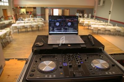 Table de mixage avec ordinateur portable et microphone dans une salle de réception aménagée avec des tables dressées.
