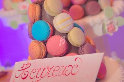 Pyramide de macarons colorés sur un présentoir, avec une carte écrite ’Heureux Mariage’ en calligraphie rouge.