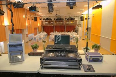 Vue depuis une régie technique avec matériel de sonorisation et éclairage, donnant sur une salle de réception décorée.