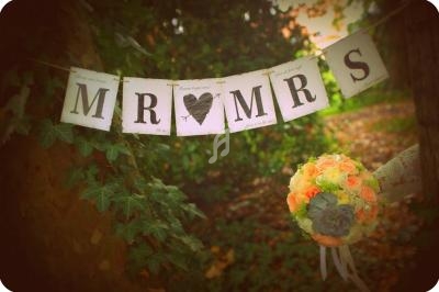 Guirlande ’Mr & Mrs’ suspendue entre des arbres, avec un bouquet de roses pastel en premier plan.