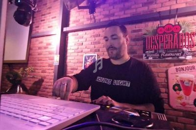 Un DJ mixe de la musique sur une console dans un bar à l'ambiance lumineuse et mur en briques.