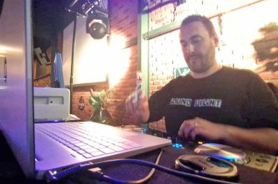 Un DJ mixe de la musique sur une console dans un bar à l'ambiance tamisée avec des lumières chaudes.