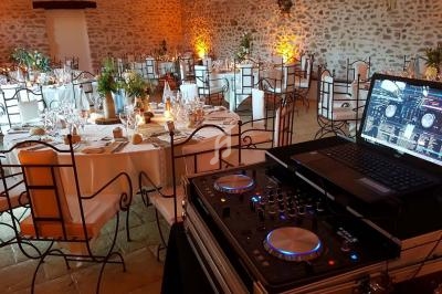 Salle de réception décorée avec des tables dressées et un poste de DJ équipé d'un ordinateur portable au premier plan.