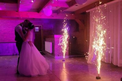 Un couple de mariés danse dans une salle illuminée par des lumières violettes et des fontaines d'étincelles.