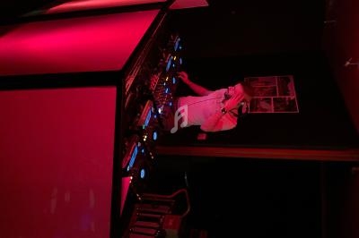 Un DJ mixe de la musique sur une table de mixage éclairée par des lumières rouges dans une salle sombre.