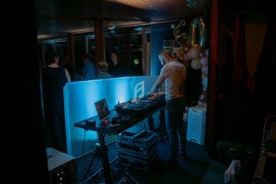 Un DJ mixe de la musique sur une table équipée de platines et d'équipements audio dans une ambiance tamisée.