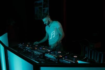 Un DJ mixe de la musique sur une table de mixage éclairée dans une ambiance sombre.