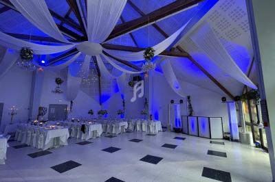 Salle de réception décorée avec des drapés blancs suspendus, éclairage bleu et tables dressées pour un événement.