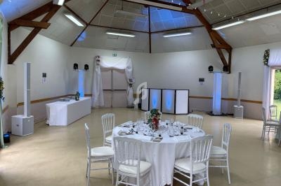 Salle de réception décorée avec des tables dressées, des chaises blanches et un éclairage discret.