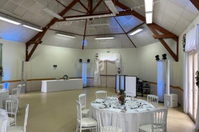 Salle de réception décorée avec des tables rondes dressées, des chaises blanches et un éclairage subtil.