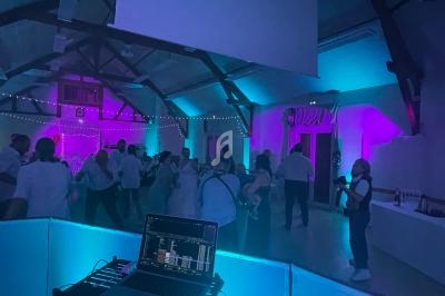 Des personnes dansent dans une salle éclairée par des lumières colorées, avec un ordinateur de DJ au premier plan.