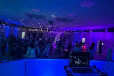 Salle de réception éclairée de lumières colorées, avec des invités dansant et un poste de DJ au premier plan.