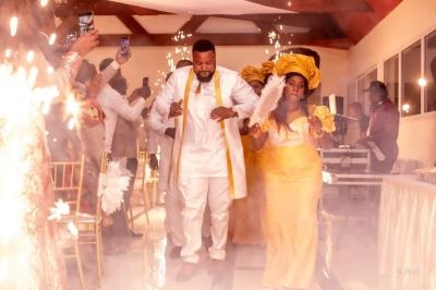 Un couple en tenue traditionnelle marche au milieu d'étincelles lors d'une célébration festive en intérieur.