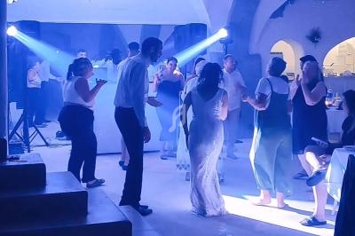 Des personnes dansent dans une salle éclairée par des projecteurs, ambiance festive avec un DJ en arrière-plan.