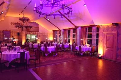 Salle de réception élégamment éclairée avec des tables rondes dressées et un grand lustre au plafond.