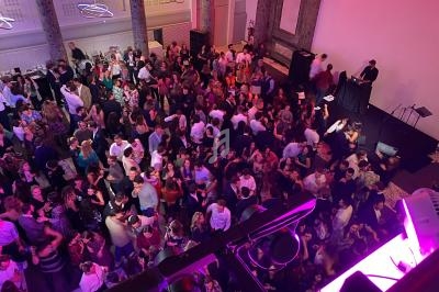 Salle bondée avec des personnes dansant et socialisant, éclairée par des lumières colorées et un DJ en arrière-plan.