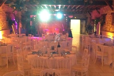 Salle de réception décorée avec des tables rondes dressées, éclairage tamisé et piste de danse en arrière-plan.