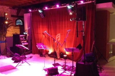 Scène de concert vide avec rideau rouge, micros sur pieds, pupitres et éclairage violet.