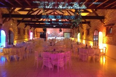 Salle de réception avec murs en briques, poutres apparentes et tables dressées sous un éclairage coloré.