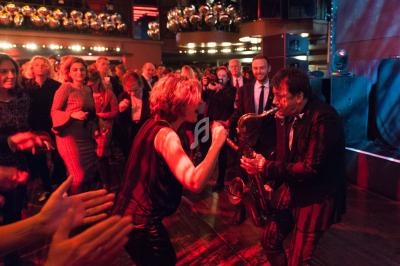 Deux musiciens jouent sur scène devant un public debout dans une ambiance festive et éclairage tamisé.