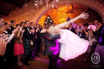 Un couple danse lors d'une réception de mariage, entouré d'invités applaudissant dans une salle éclairée chaleureusement.