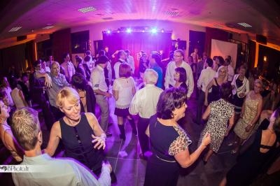 Personnes dansant lors d'une soirée festive dans une salle éclairée par des lumières colorées.