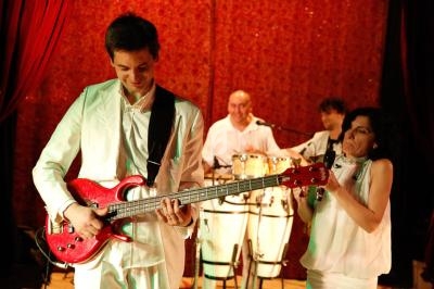 Un groupe de musiciens en tenue blanche joue sur scène, avec un guitariste au premier plan.