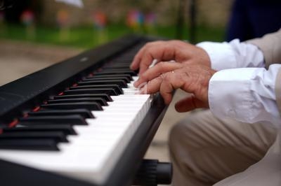 Mains d'une personne jouant sur un clavier de piano électronique dans un environnement extérieur flou.