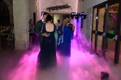 Deux couples dansent sur une piste entourée de fumée et éclairée par des lumières colorées dans une salle festive.