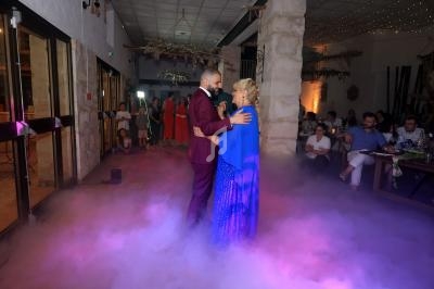 Un couple danse au milieu d'une piste entourée de fumée, dans une salle décorée avec des invités en arrière-plan.